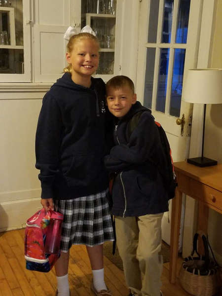 A brother and sister wearing warm clothes, going back to school on a cold day