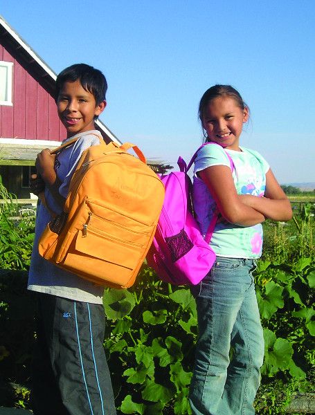 Two kids posing with their new backpacks outside