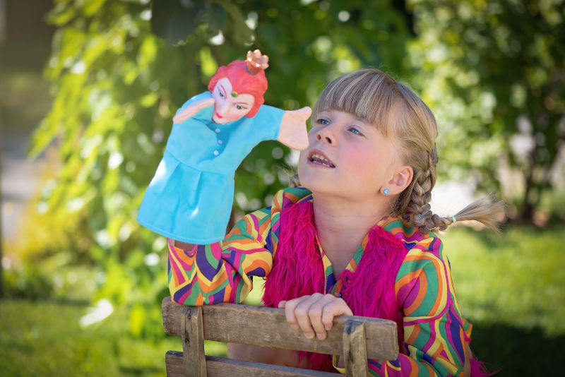 A blond girl plays with a puppet outdoors A blond girl plays with a puppet outdoors