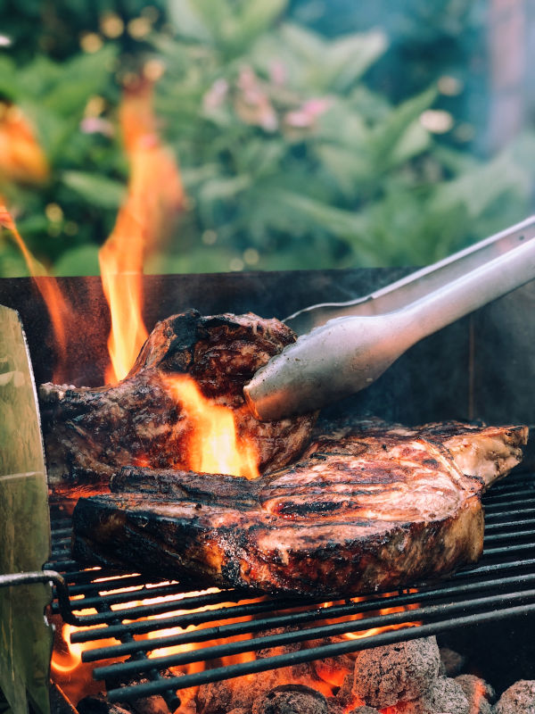 Grilling tongs flip steaks over a fiery grill